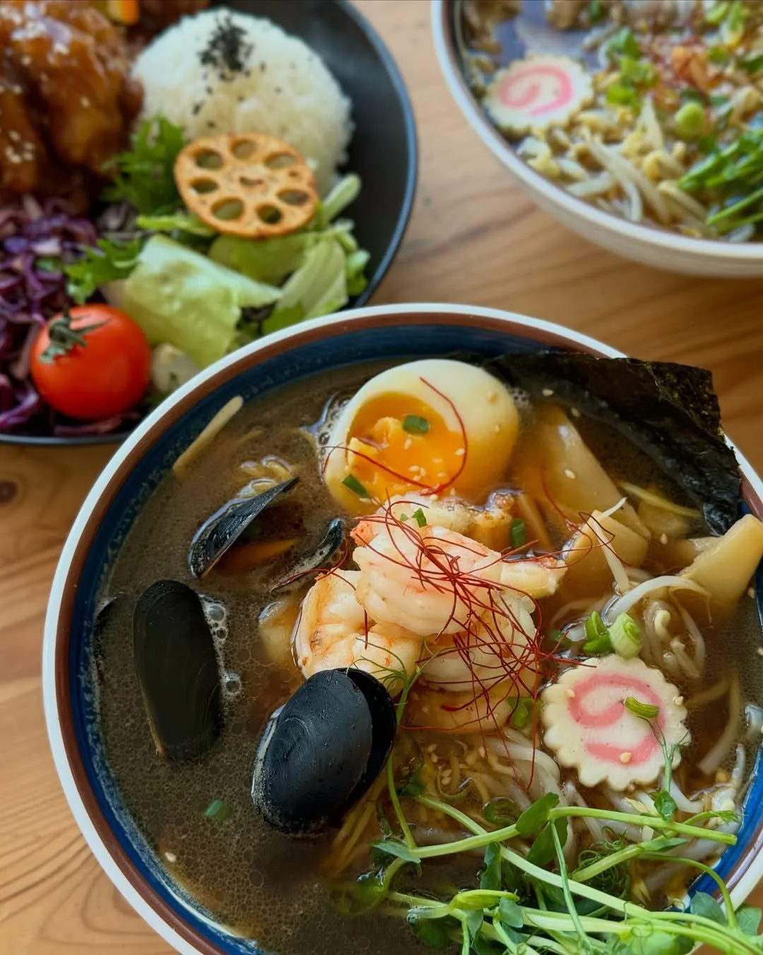 Ramen ar garnelēm, mīdijām, olu un zaļumiem, fonā rīsi ar salātiem